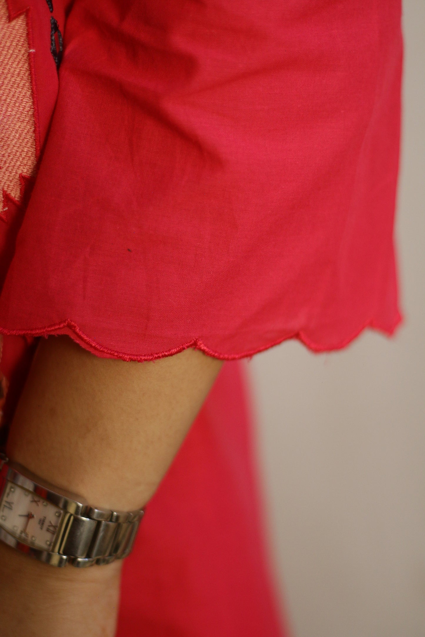 Close-up of a person wearing a red skirt with a scalloped edge and a watch on a neutral background.