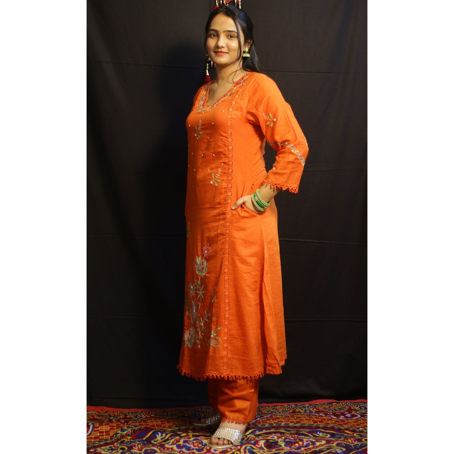 Woman wearing an orange traditional outfit with embroidery against a black background