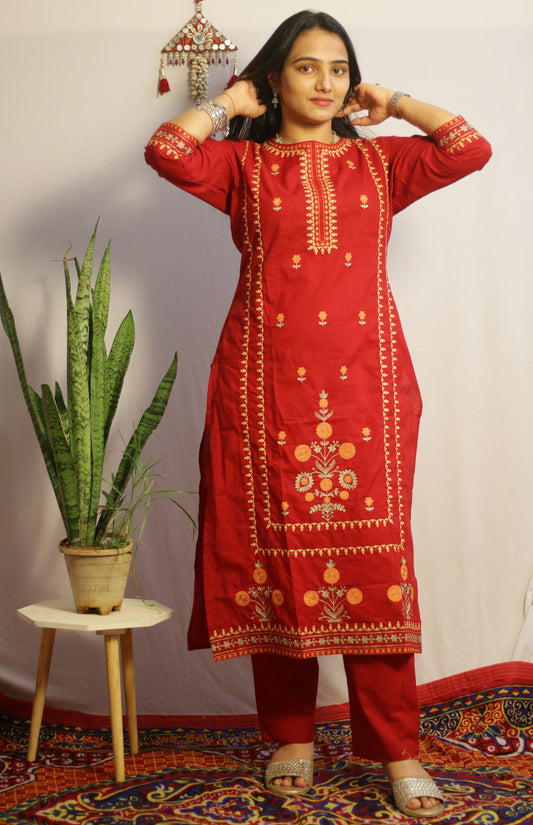 Woman wearing a red embroidered kurta with a plant and decorative wall hanging in the background