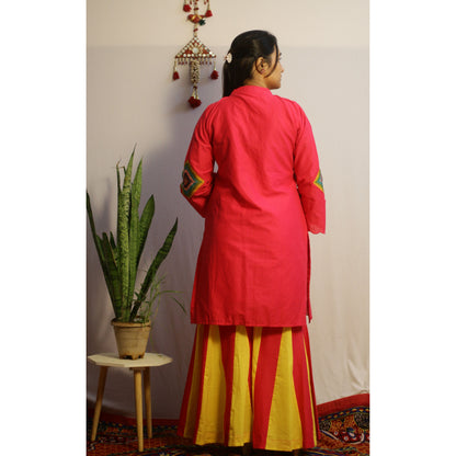 Person wearing a red kurta with yellow pants standing against a white wall.