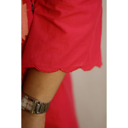 Close-up of a person wearing a red skirt with a scalloped edge and a watch on a neutral background.