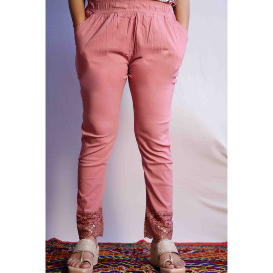 Pink pants with lace trim worn by a person on a colorful rug.