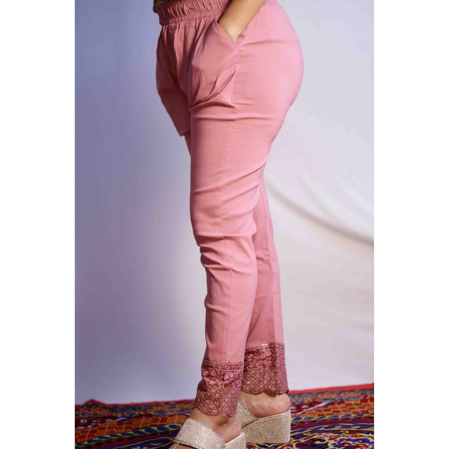 Pink pants with lace trim worn by a person on a colorful rug.