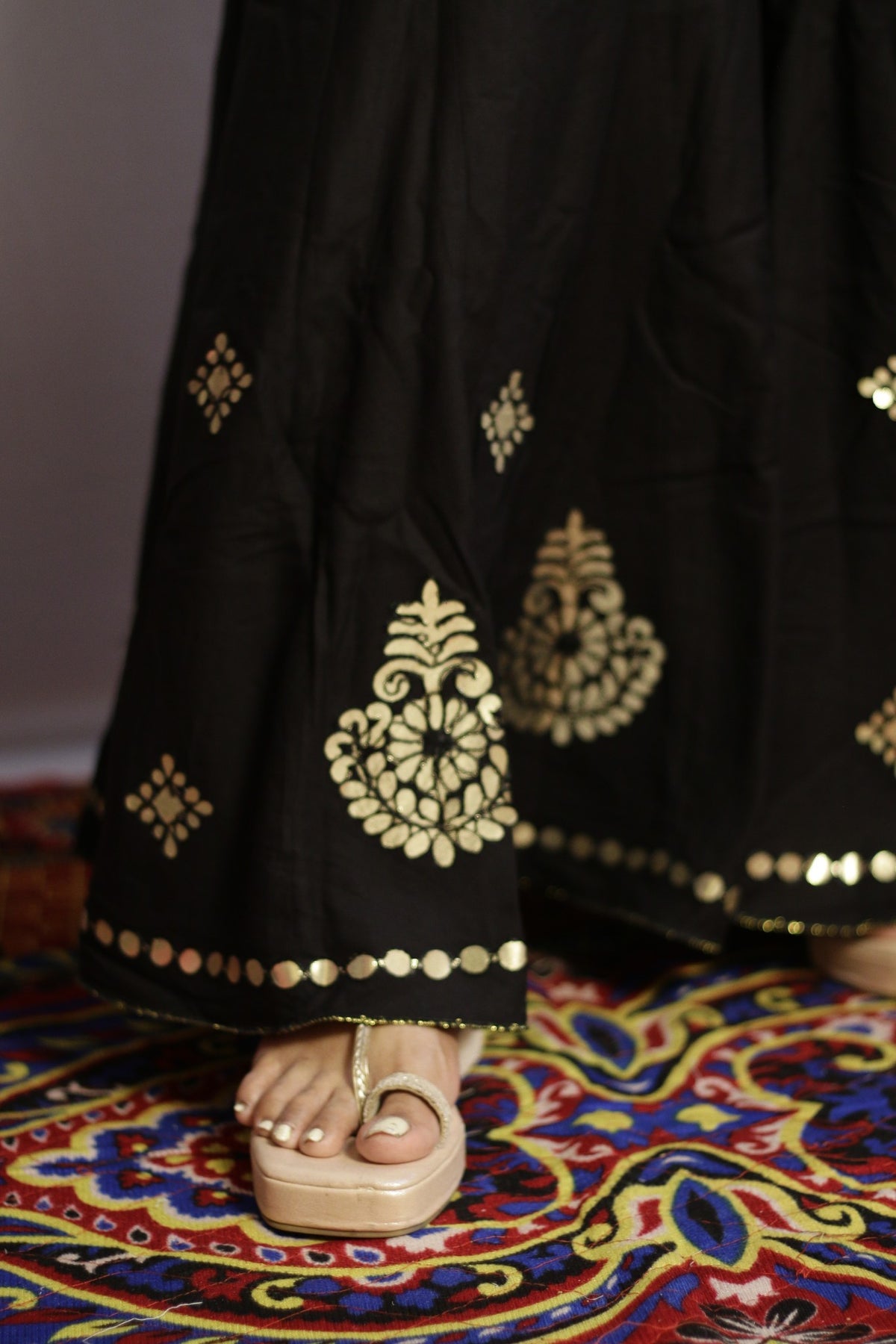 Close up of gold gotta patti paisley motifs and disc trim on the black palazzo hem