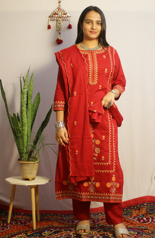 Woman wearing a red traditional outfit with gold embroidery in a decorated room.