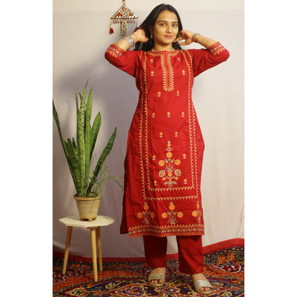 Woman wearing a red embroidered kurta with a plant and decorative wall hanging in the background